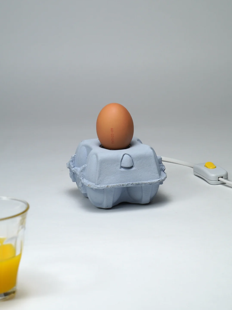 EggboxLAMP Sky LED lamp met een ei op een grijze eierdoos, met aan/uit-schakelaar en glazen sap.