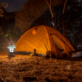 Aigostar oplaadbare LED campinglamp naast een tent in een donkere bosomgeving
